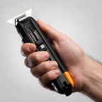 Hand holding the retractable utility knife positioned in scraper mode with the wide horizontal blade exposed.