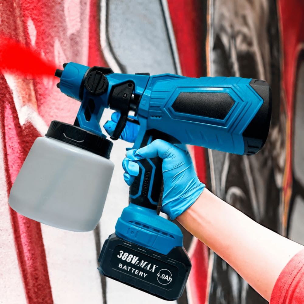 Gloved hand operating a blue cordless paint spray gun applying red paint against an outdoor wall.